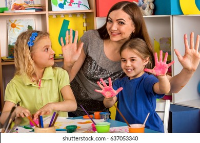 Small Students With Teacher Finger Painting In Art School Class. Teacher Cheers Children In Kindergarten. Mom And Daughters At Home. Craft Drawing Education Develops Creative Abilities Of Children.