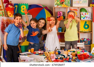 Small Students With Teacher Finger Painting In Art School Class. Teacher Cheers Children In Kindergarten. Mom And Kids At Home. Craft Drawing Education Develops Creative Abilities Of Children.