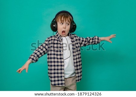 small stylish boy, a 4-5-year-old kid in a plaid shirt and a white t-shirt with a cap on his head dances with his arms outstretched, on an isolated green background