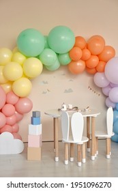 Small Table And Chairs With Bunny Ears In Children's Room Interior. Rainbow, Colorful Balloon Arch, Decoration In Honor Of The Holiday, Birthday, Party