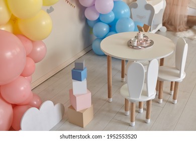 Small Table And Chairs With Bunny Ears In Children's Room Interior. Rainbow, Colorful Balloon Arch, Decoration In Honor Of The Holiday, Birthday, Party