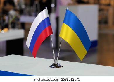 Маленькие столовые флаги России и Украины вместе на каком-то мероприятии. Флаги двух стран как символ сотрудничества между двумя государствами. Совместный бизнес Украины и России