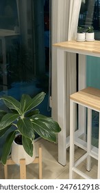 A small table and stool set with a plant in a pot in front of a window.