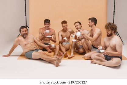 Small Talks. Group Of Happy Cheerful Men Of Different Ages And Body Shapes Sitting On Floor And Drinking Tea At Studio Photo Shoot. Feeling Comfortable. Fashion Models Shirtless