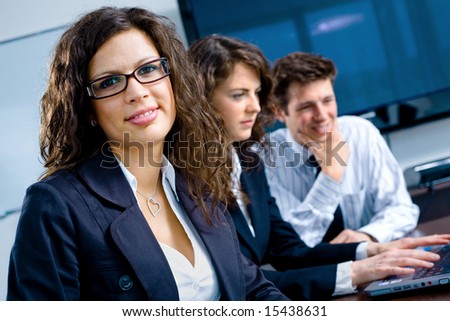 Small team of young businesspeople working together at meeting room at office. Huge plasma TV screen in background.