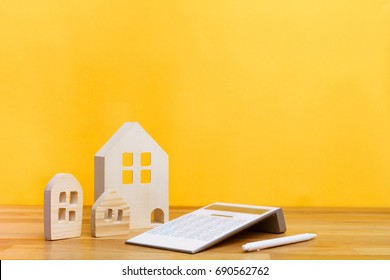 Small Three Wooden Houses With Modern Design White Calculator And White Pen On Yellow Background For Home Loans Concept