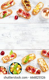 Small Toasts (crostini) With Cream Cheese And Cut Fresh Fruits (pear, Peach, Cherry, Grilled Figs) On White Table. Top View Of Summer Appetizers With Place For Text. 