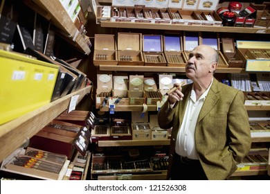 Small Tobacco Store Owner Looking At Cigar Boxes On Display In Shop