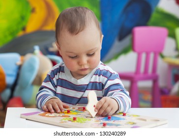 Small toddler or a baby child playing with puzzle shapes on a low table in a colorful children room in a nursery or preschool.
