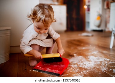 A small toddler girl with brush and dustpan sweeping floor in the kitchen at home. - Powered by Shutterstock