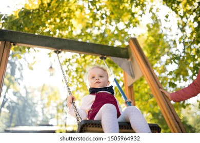 A small toddler girl with unrecognizable father on a swing on a playground. - Shutterstock ID 1505964932
