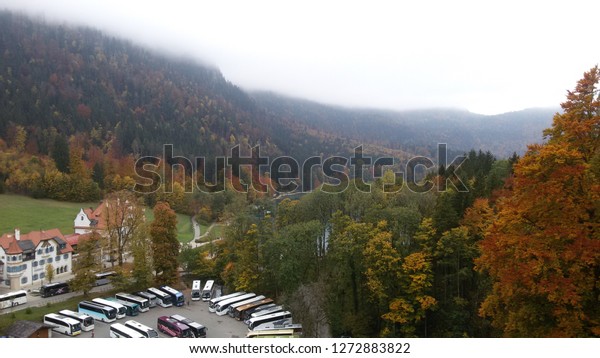 A small\
town in germany with tourist buses and cars in parking lot by a\
lakeside surrounded by trees with Autumn\
leaves