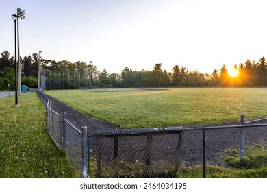 Small town suburb green grassed baseball field with metal fence, dug outs and tall flood light at sunrise in rural town Ontario Canada - Powered by Shutterstock