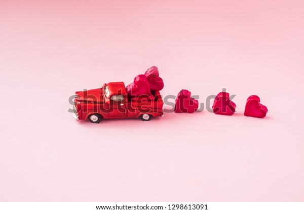 A small toy car carries candy in the shape of\
hearts on a pink background. Valentine\'s day concept. greeting\
card.Love.selective focus