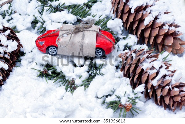 small toy car packed as a gift and cones\
on spruce branches covered with artificial\
snow