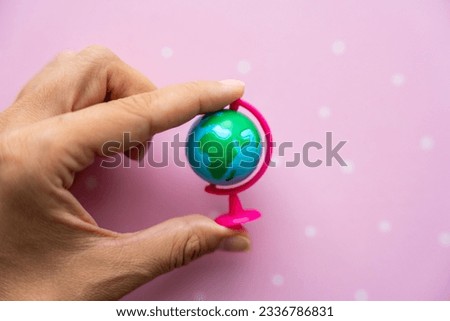 Small toy globe in woman hand on a pink background. High quality photo