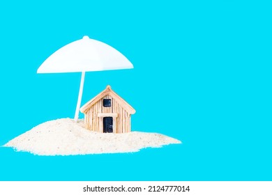 Small toy house in a pile of sand under a white parasol isolated on blue. Creative home protection concept. - Shutterstock ID 2124777014