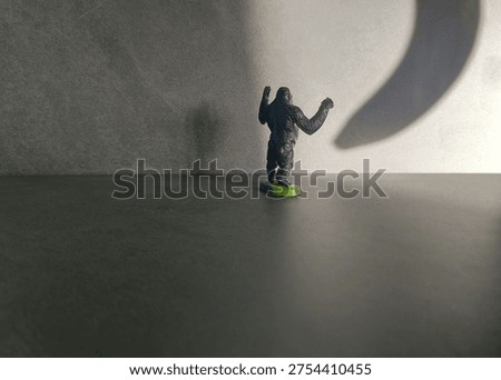 Small toy monkey looking at a large banana shadow on a wall symbolizing temptation, craving, desire or humorous food concept with copy space
