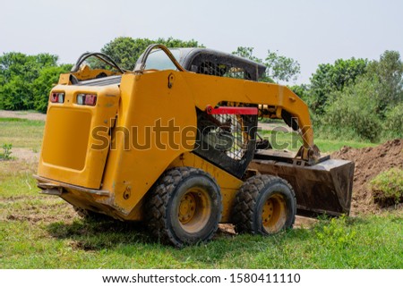 Small tractor digging dirt with grass, the tractor is on its back.