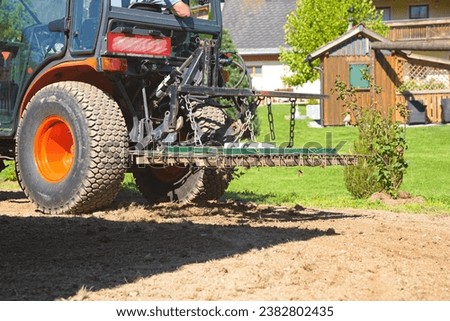 Small tractor with tine harrow working on soil - harrowing