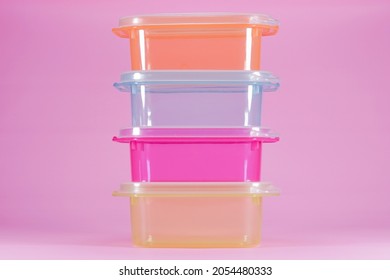 Small transparent plastic container for storing food. Four colorful transparent plastic containers stacked on isolated pink background. Food grade material.