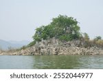A small tree grows on a limestone island in the middle of the water, casting shadows in the still water.