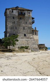 a small tree next to an old stone castle on the beach, blue sky  and footprints in the sand