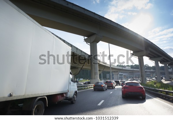 small\
Truck and cars on road. Blue sky and\
overpass.