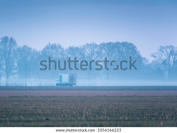 Small truck driving on misty country road in\
early morning.