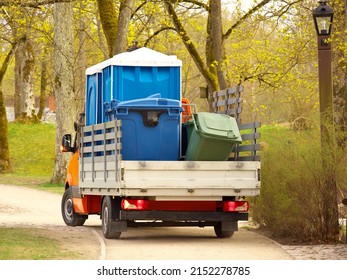 A Small Truck Is Driving In The Park. Two Cabins Of Dry Closets And Garbage Containers Are Transported By A Car. Selective Focus.