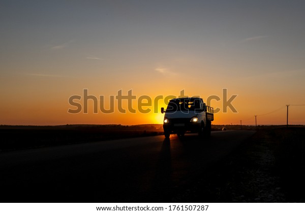 A small truck with its lights on is\
driving along the road. The background image is the sky in red and\
yellow from the setting sun. Contour\
image.