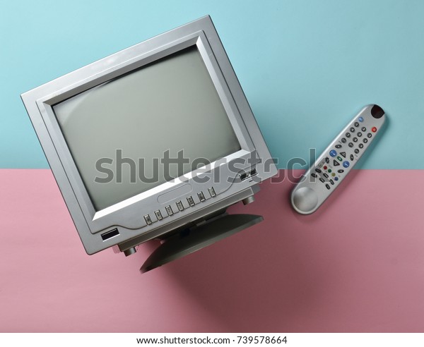 A small tube black and white\
TV and a remote control on a pink blue pastel background. Top\
view.
