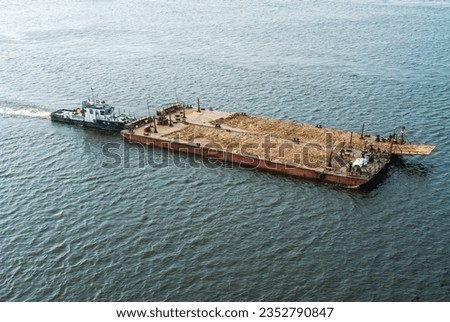 A small tugboat pushes a large barge without cargo on a wide river. Summer navigation on the river. Cargo transportation. River vessels on the river.  Water transport.