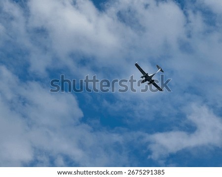 Small twin-engine propeller airplane flying high in the sky among scattered clouds on a sunny day.