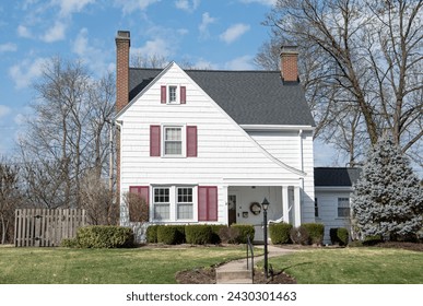 Small, two-story, white house with sloping roofline and red shutters.