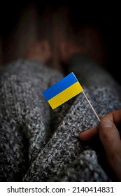 Small Ukrainian national flag in woman's hand on the knitted grey background copy space 
