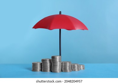 Small umbrella and coins on light blue background