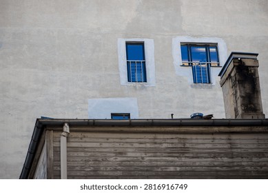 Small upper floor windows with blue reflections appear above an aged wooden rooftop, forming a layered urban architectural scene with contrasting materials.