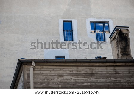 Small upper floor windows with blue reflections appear above an aged wooden rooftop, forming a layered urban architectural scene with contrasting materials.