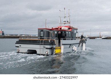 Small utility work boat navigating through a coastal harbor area. The vessel is used for port services, maritime operations, and harbor support activities, representing marine logistics, coastal transportation, and industrial port infrastructure.