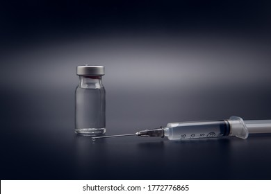 Small Vaccine Bottle (phial) And A Medical Syringe Injection With A Vaccine Drop On Its Needle, Isolated On Black Background Vaccination For Prevention, Immunization And Treatment To Infections