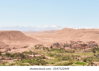 A small village nestled in a desert landscape with distant snow-capped mountains under a clear blue sky. - Powered by Shutterstock