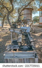 Small Vinatge Wood Water Storage Tank With Metal Pipe And Wooden Waterway. Old Water Barrel Against A Scenic Landscape Of Lake Austin, Trees, And Blue Sky On A Sunny Day In Texas.