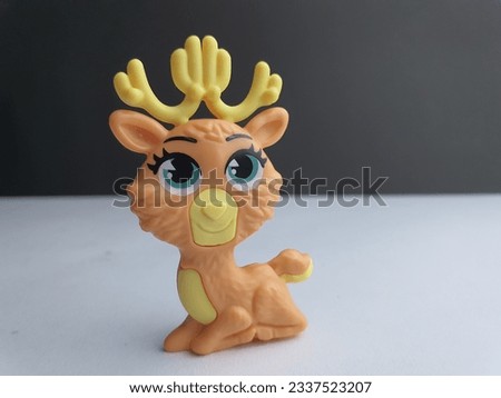 Small vinyl figurine toy of a cute deer laying on white surface background.