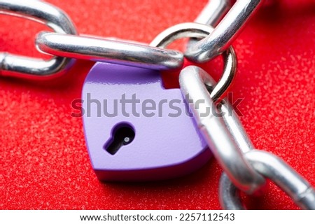 Small violet lock in shape of heart linked to the chain. Heart lock holding three pieces of chain. Concept of love