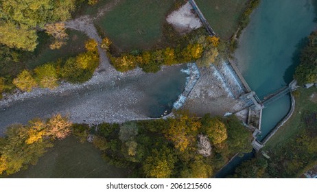 Small Water Dam Or Flood Prevention Visible From Above. Irrigated River Seen From A Drone Perspective, River And Trees Around.