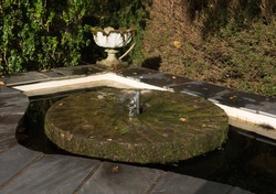 Small Water Fountain Coming Up Through An Old Mill Stone In A Pond In A Country Cottage Garden In Rural Devon, England, UK