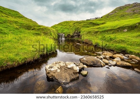 Small waterfall coming down from the mountain in an idyllic green landscape on the Isle of Skye, Scotland.