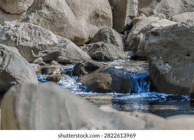 A small waterfall flow hidden between smooth natural boulders in a forest stream. Peaceful focus on clean water moving over rocks.