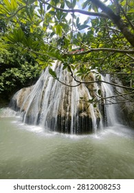 a small waterfall flowing down a limestone cliff in front of the mouth of a cave.